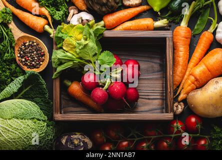 Radish and carrot fresh bunch in old wooden box and fresh farm organic vegetables on rustic black concrete background. Autumn harvest, vegetarian Stock Photo