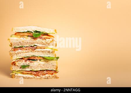 Close up of tall cut tasty sandwich with cheese, ham, prosciutto, fresh lettuce, tomatoes, cucumbers on pastel yellow background. Healthy gourmet Stock Photo
