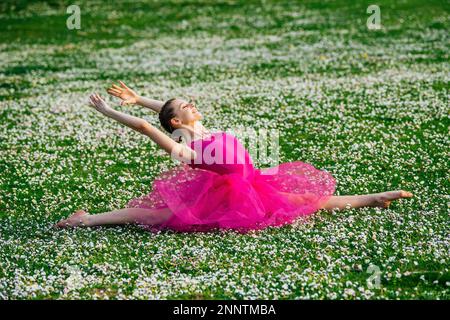 Ballerina doing splits on lawn with flowers, Battle Point Park, Bainbridge Island, Washington, USA Stock Photo