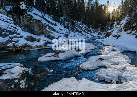 River flowing through snow covered forest in winter, Spray River, Canmore, Alberta, Canada Stock Photo