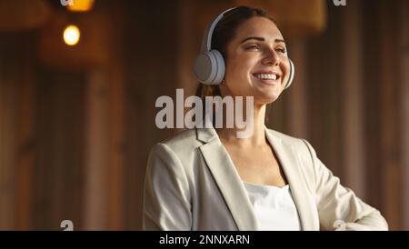 Happy business woman wearing wireless headphones in an office. Professional business woman listening to a music playlist at work. Stock Photo