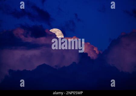 Purple clouds and full moon at sunset Stock Photo