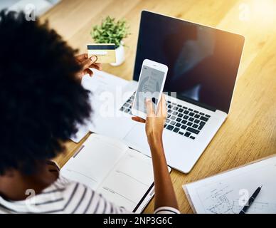 Lets see what social media is doing. Over the shoulder shot of a unrecognizable woman using her cellphone and working on her laptop at home. Stock Photo