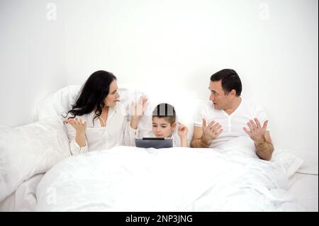 home disagreements parents quarrel in bed under covers son boy with tablet in hands family violence inattention to children a lonely child not pedagogical education psychological problems conflicts Stock Photo