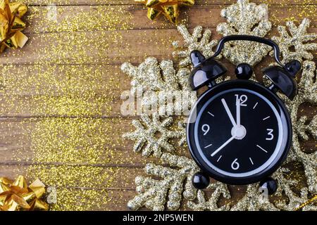 Retro style clock counting last moments before Christmass or New Year, on vintage wooden background with golden sparkles glare and bows. Concept Chris Stock Photo