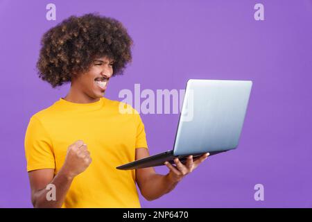 African man with curly hair celebrating while using a laptop Stock Photo