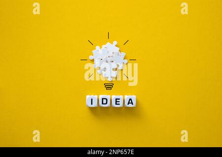White puzzle pieces creating a light bulb illustration with the word idea on a yellow background Stock Photo