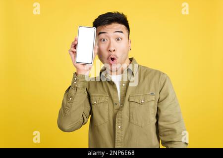Surprised chinese man holding a mobile with a blank screen Stock Photo