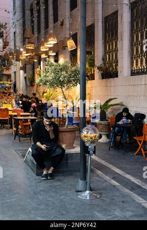 Amman, Jordan - October 23 2022: Arabian Man Smoking a Cigarette and looking at Smartphone at Night in the City Stock Photo