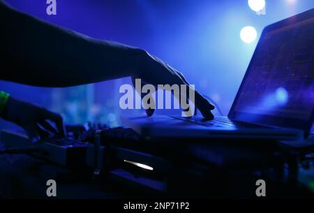 Club DJ playing music with laptop and midi controller. Hand of professional disc jockey mixing musical tracks on party in night club Stock Photo