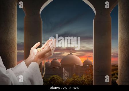 Muslim man praying with prayer beads in his hands with mosque background Stock Photo