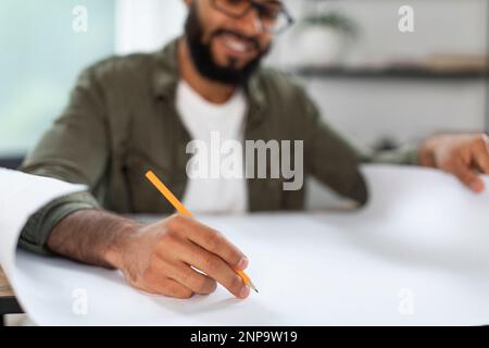 Black man engineer in glasses working with drawings at workplace at home office interior, selective focus on hand Stock Photo