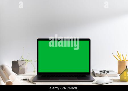 Chroma key green screen laptop on table of designer in front of white backgroud. Table top shot of interior space with window light effect. Stock Photo