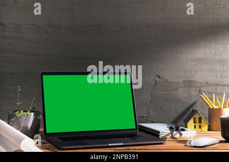 Chroma key green screen , angled view laptop on wooden table in front of concrete wall. Table top shot of interior space with window light effect. Stock Photo