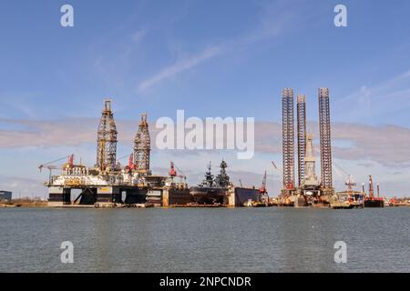 Galveston, Texas, USA - Febriuary 2023: Oil rigs in the city's port for maintenance and repair, with the historic USS Texas warship being restored in Stock Photo