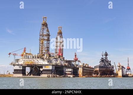 Galveston, Texas, USA - Febriuary 2023: Oil rigs in the city's port for maintenance and repair, with the historic USS Texas warship being restored in Stock Photo