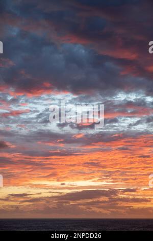 Dramatic twilight with the sun gradually setting over the tranquil ocean while covering the entire sky with a stunning spectrum of colors Stock Photo