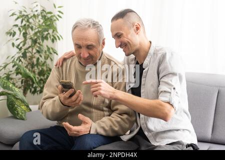 Happy two generations male family old senior mature father and smiling young adult grown son enjoying talking chatting bonding relaxing having Stock Photo