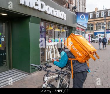 A just eat delivery cyclist waits outside a McDonalds. Stock Photo