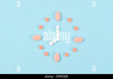 Clock created from pink and white pills on blue background. Right time for using medicines. Stock Photo