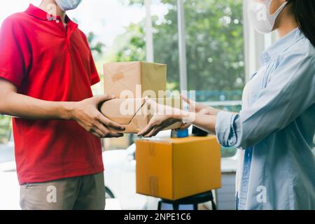 Asian delivery man wearing face mask in red uniform deliver service parcel box to woman customer at home Stock Photo