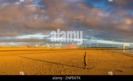 The setting sun over the Irish Sea creates a long shadow behind one of the Iron Men at Another Place on Crosby Beach. Stock Photo