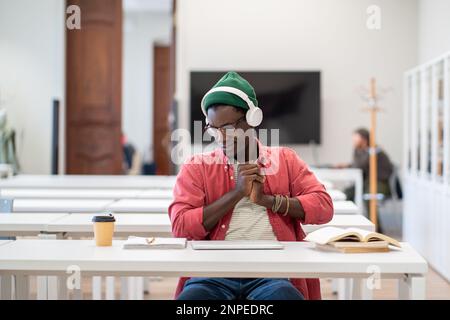 Tired sleepy black guy student in headset stretch on chair exhausted after long time study at laptop Stock Photo
