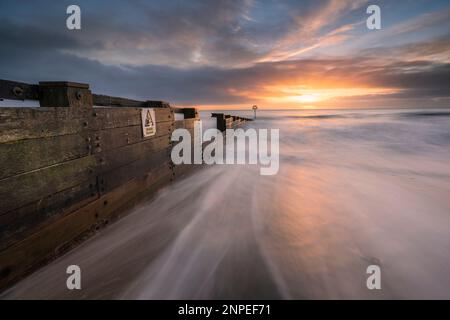 Waves washing around a groyne on a beach at sunrise. Stock Photo