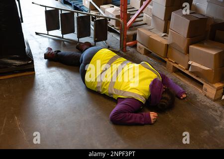 Accident in the work place, young woman lies injured after falling from step ladder onto the factory floor Stock Photo