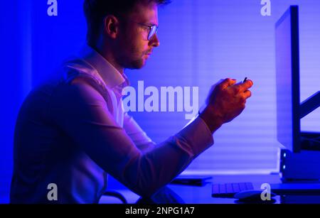 Caucasian Man in His 30s Browsing His Smartphone in Front of Desktop Computer. Mobile Applications Theme. Stock Photo