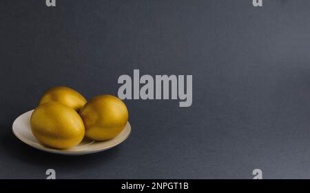 Three gold eggs on white saucer with gold border on dark gray background. Stock Photo