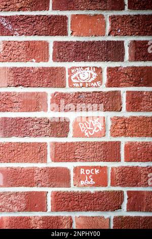 Close up of red brick wall with small pieces of white painted graffiti Stock Photo