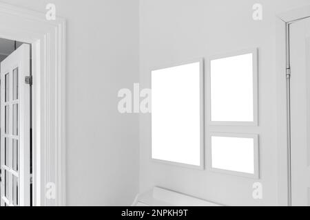 Three white wooden picture frames with mockup space for photography hanging on living room wall, selective focus Stock Photo