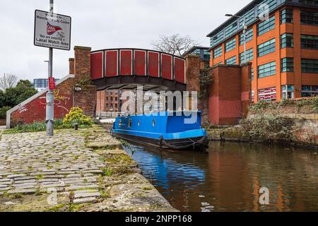 A blue narrow boat passes under the pretty red Kitty footbridge in the Ancoats area of Manchester in 2023. Stock Photo