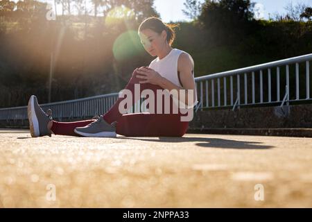 Woman runner sitting on the road holding her knee, sports injury Stock Photo