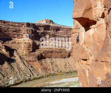 Adult male climber ascends a cliff above the Colorado River, Utah. Stock Photo