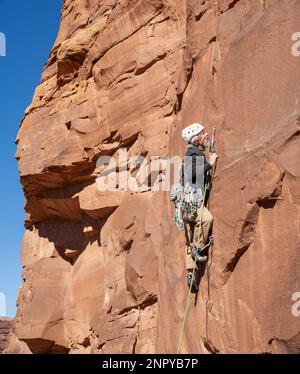 Adult male ascends a steep rock face. Moab, Utah Stock Photo