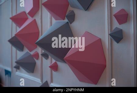 Abstract background of paper polygons of gray, pink, different shapes on a white wall. Creative home decor. Dynamic figures in the interior. Origami h Stock Photo