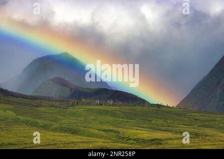 Low hanging glowing rainbow across the west maui mountains. Stock Photo