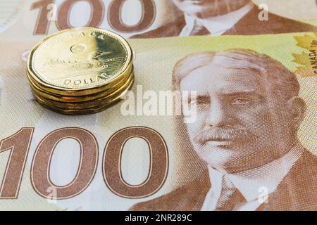 Stack of Canadian one-dollar coins on top of Canadian one-hundred dollar bank notes. Stock Photo