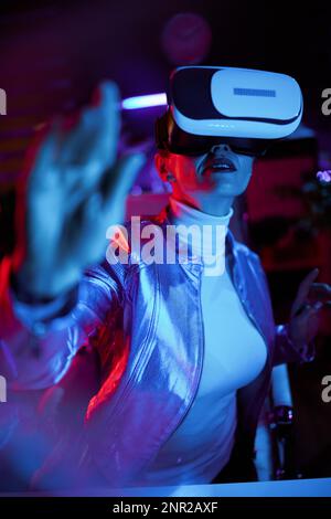 Neon metaverse futuristic concept. elegant business woman in virtual reality goggles testing out metaverse in modern office. Stock Photo