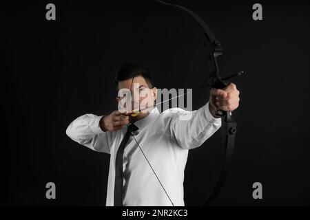 Businessman with bow and arrow practicing archery on black background Stock Photo