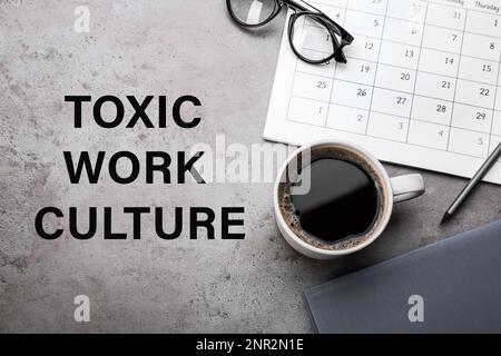 Cup of coffee, computer keyboard, stationery and text TOXIC WORK CULTURE on grey table, flat lay Stock Photo