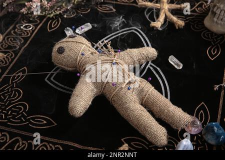 Voodoo doll with pins and dried flowers on table Stock Photo