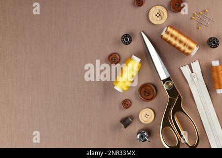Different sewing supplies on brown fabric, flat lay. Space for text Stock Photo