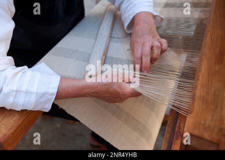 Close up on the hands of a man weaving a canvas from flax fibers with an antique hand weave machine. Stock Photo