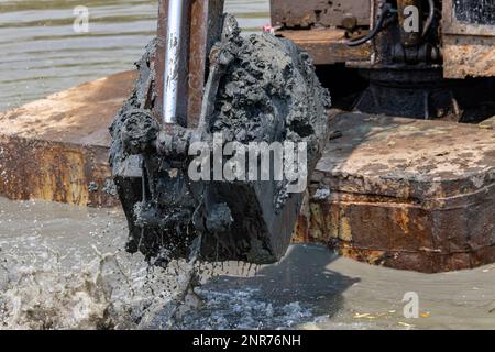 Dredging the bottom of water area, view of the bucket of the floating excavator full of mud Stock Photo