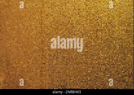 Small gold tile texture. Small golden tiles arranged to fit it into background. Shiny golden mosaic background with small square, glazed tiles in rows Stock Photo