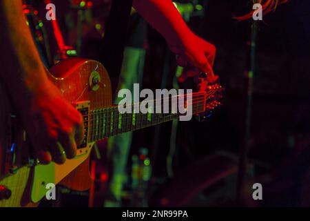 The guitarist tunes the guitar holding on to the peg in the spotlight. Guitar Tuning Stock Photo