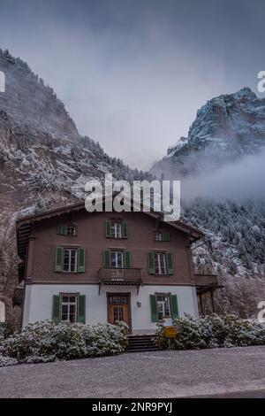 Roadside cottage or hotel or palace next to a road in Lauterbrunnen valley on a cloudy winter day with some haze in the air. Stock Photo